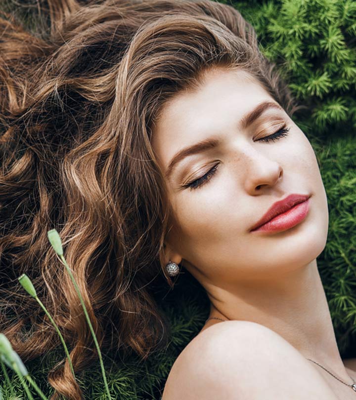 A woman with frizzy hair with a greenery background A woman with frizzy hair with a greenery background