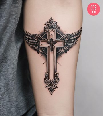 A black and gray cross tattoo with wings inked on the forearm A black and gray cross tattoo with wings inked on the forearm